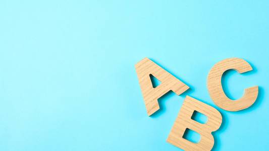 Die Buchstaben A B und C aus Holz auf blauem Hintergrund.